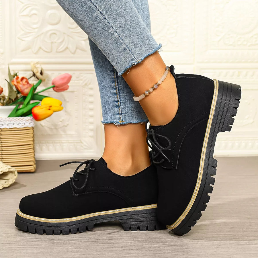 Black lace-up shoes worn with light blue jeans on a neutral background