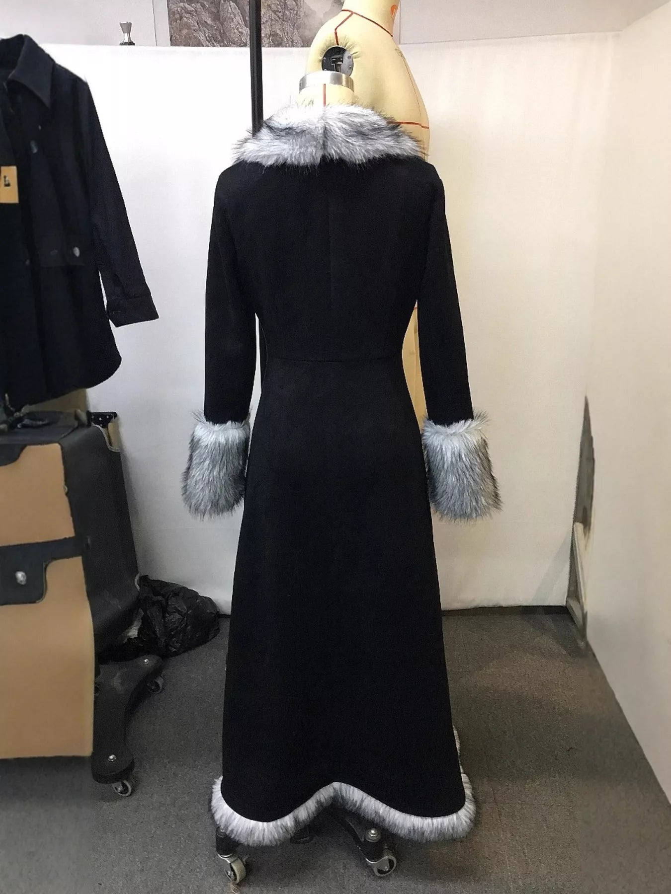 Black coat with fur trim on a mannequin against a white wall.