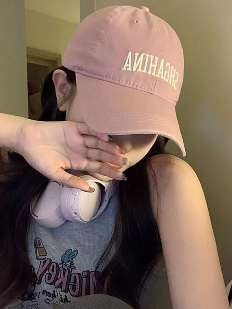 Person wearing a pink cap with 'SHEHANNA' text, covering their face.