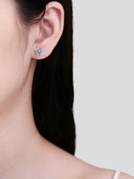 Close-up of a person wearing diamond stud earrings with a plain background