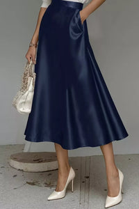 Person wearing a navy satin skirt with white shoes on a gray background