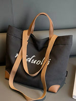 Black tote bag with brown handles and strap on a gray surface