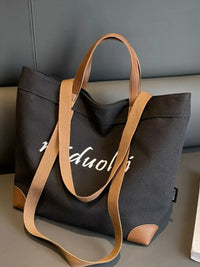 Black tote bag with brown handles and strap on a gray surface