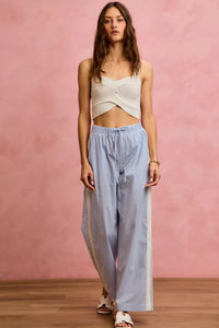 Woman wearing a white top and light blue checkered pants against a pink wall.