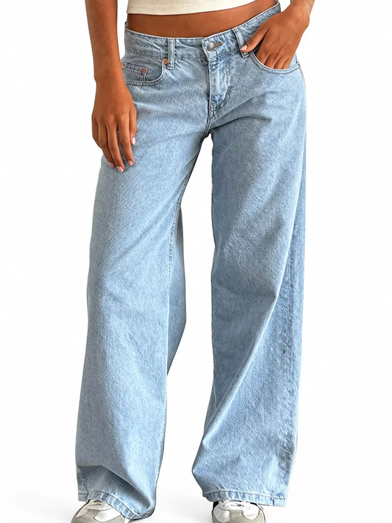 A person wearing light-wash, wide-leg denim jeans with a cropped beige top and white sneakers, shown from the waist down against a plain white background.
