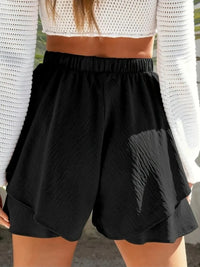 Person wearing a white cropped top and black shorts with a blurred background