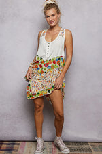 Woman wearing a white sleeveless top and colorful floral skirt against a plain background