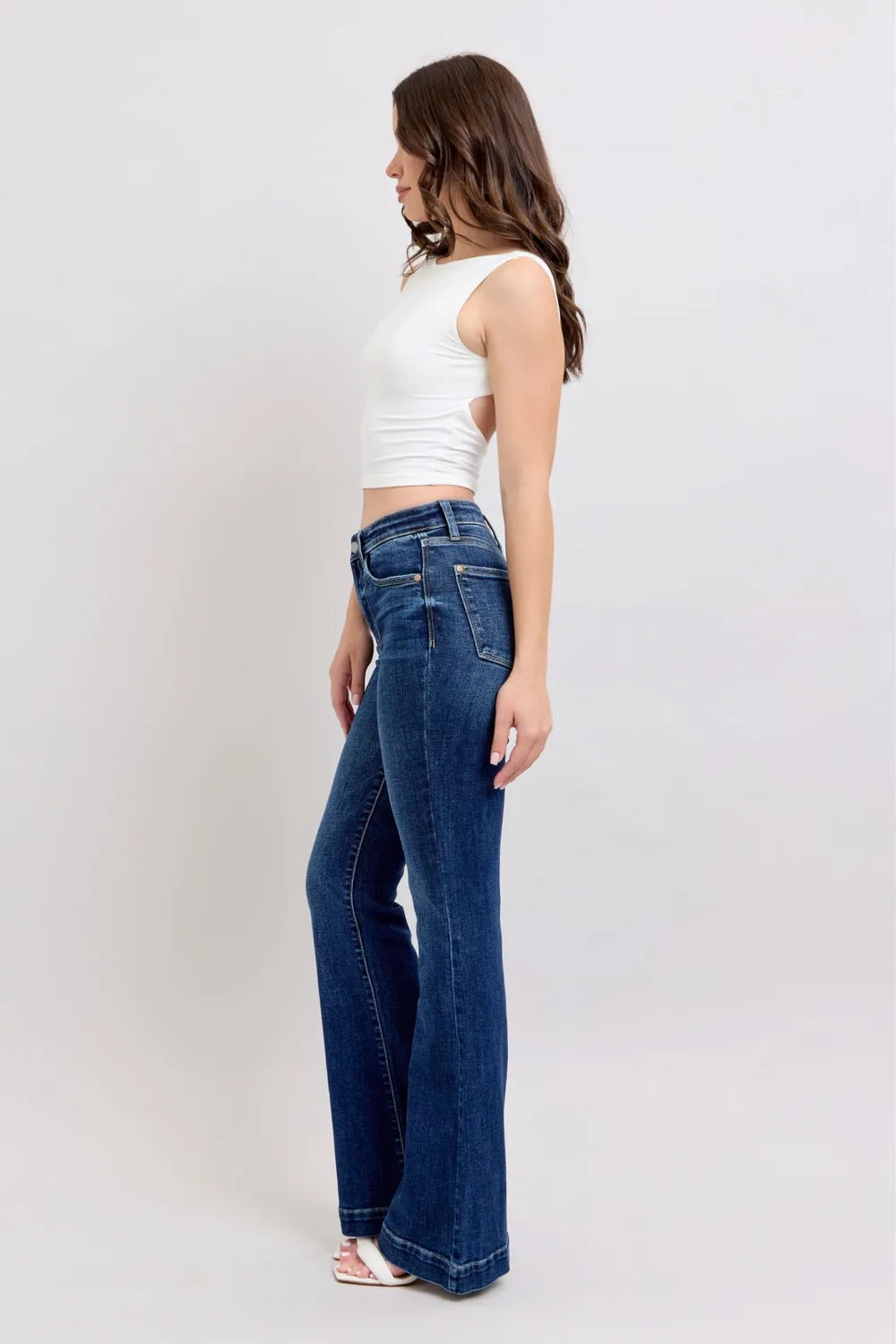 Woman wearing blue jeans and a white top on a plain background