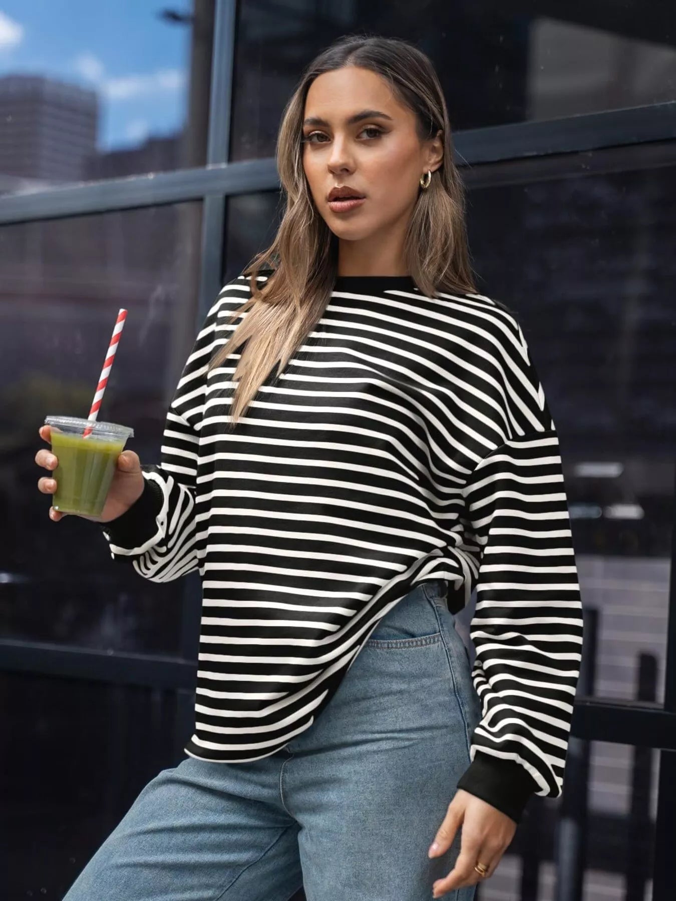 Woman in a black and white striped sweater holding a green smoothie.