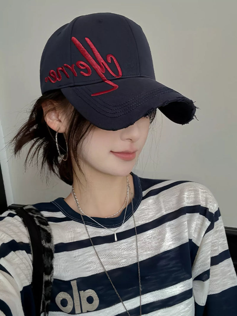Person wearing a navy cap with red text and a striped shirt.