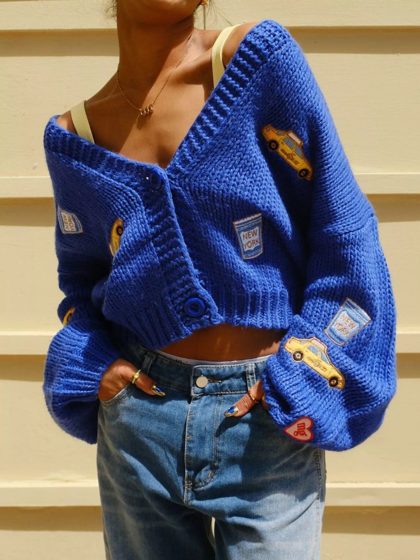 Person wearing a blue knitted cardigan with patches and jeans on a striped background