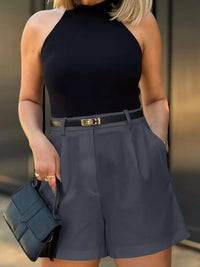 Person wearing a black sleeveless top and gray shorts, holding a matching handbag.