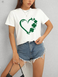 Person wearing a white t-shirt with a green heart and shamrock design, paired with denim shorts.