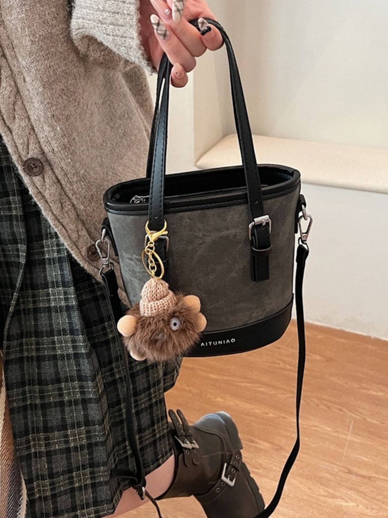Person holding a gray handbag with a bear keychain, wearing a plaid shirt and brown shoes.