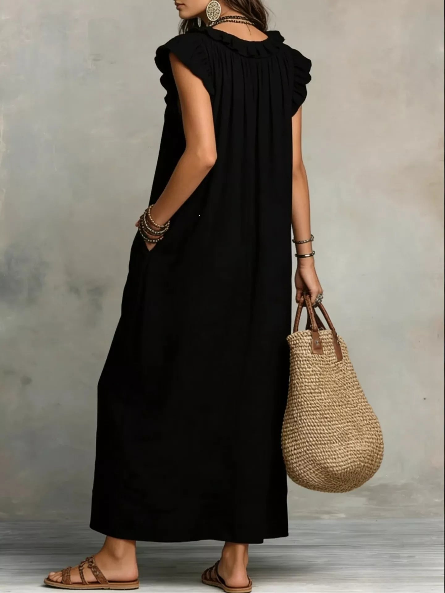 Person wearing a black dress holding a woven bag against a neutral background