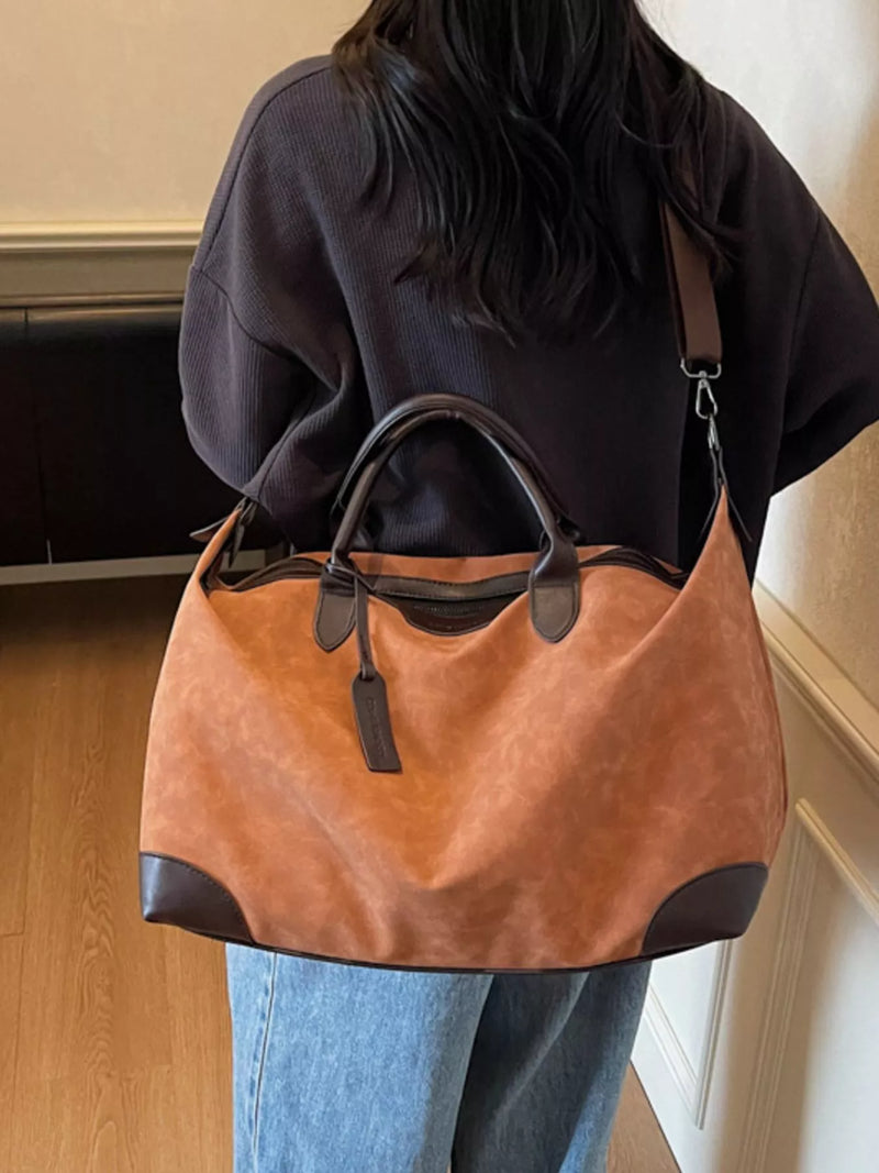 Person holding a brown leather handbag with black accents indoors.