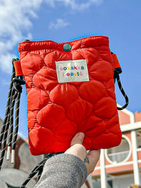 Red puffer bag with a visible brand label held against a blue sky.