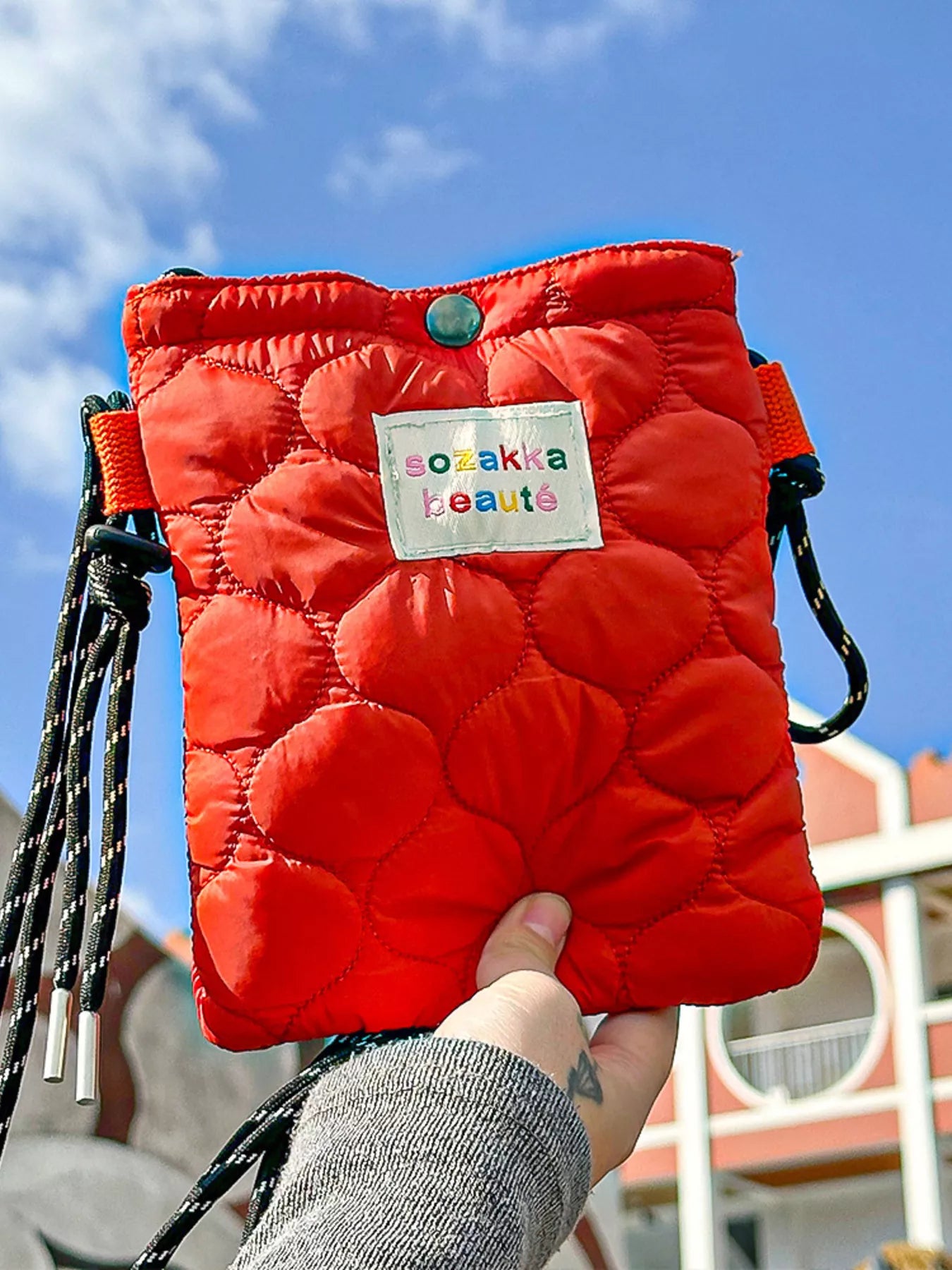 Red puffer bag with a visible brand label held against a blue sky.