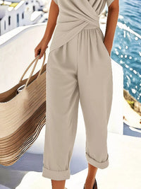 Woman in beige outfit holding a straw bag by water