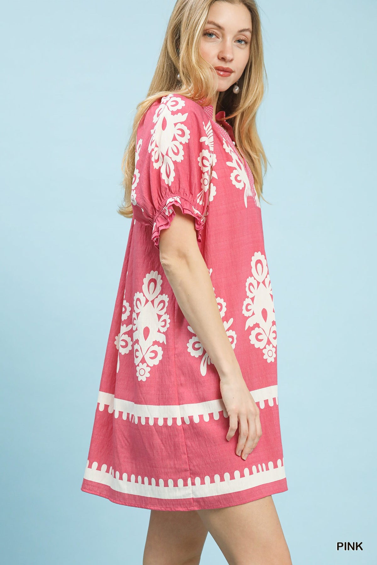 Woman wearing a pink dress with white patterns on a light blue background