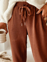 Brown ribbed pants with a drawstring waist worn by a person holding a mug.