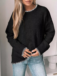 Person wearing a black sweater with white trim and light blue jeans against a neutral background