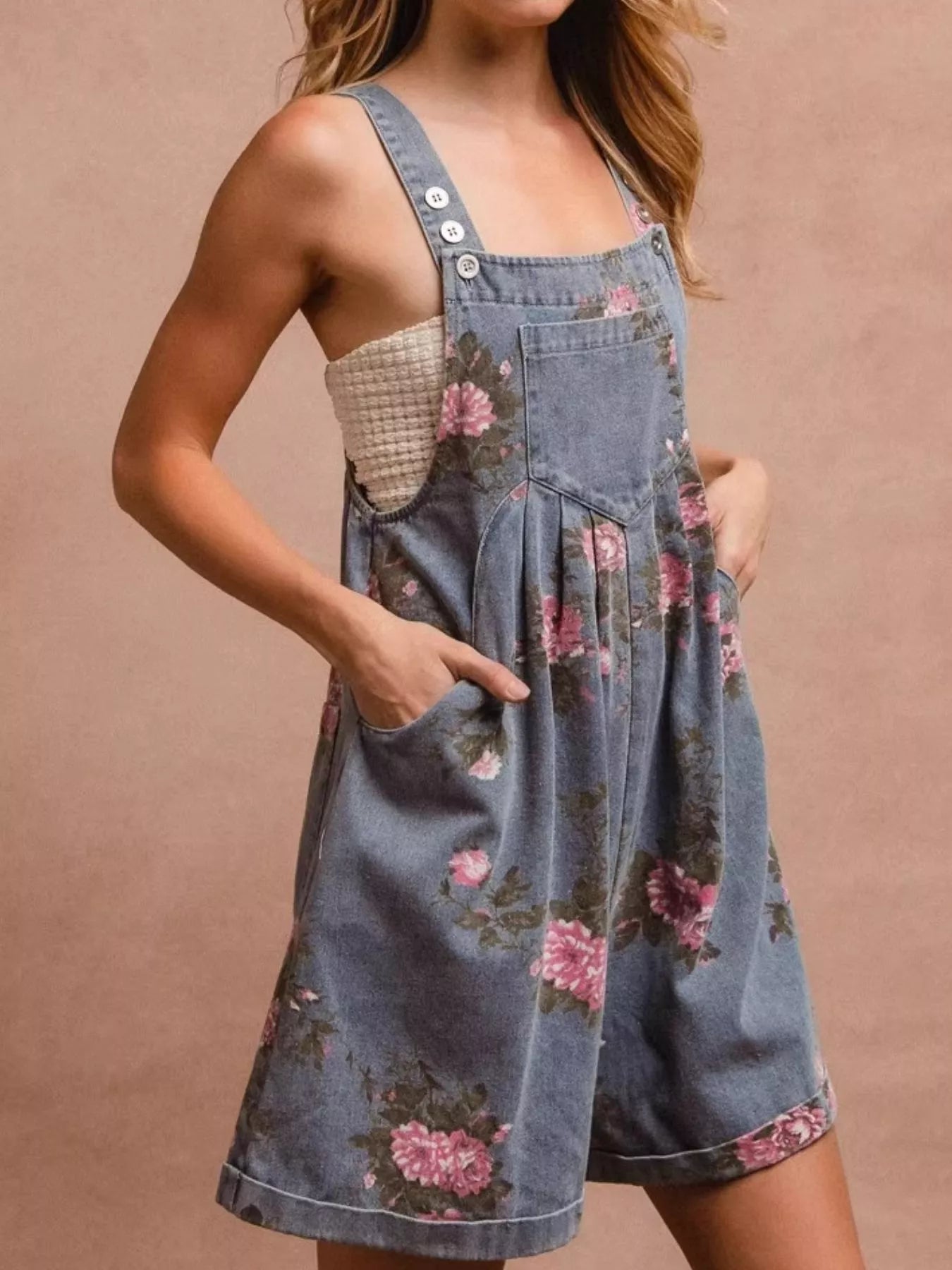 Denim overalls with floral pattern worn by a person on a beige background