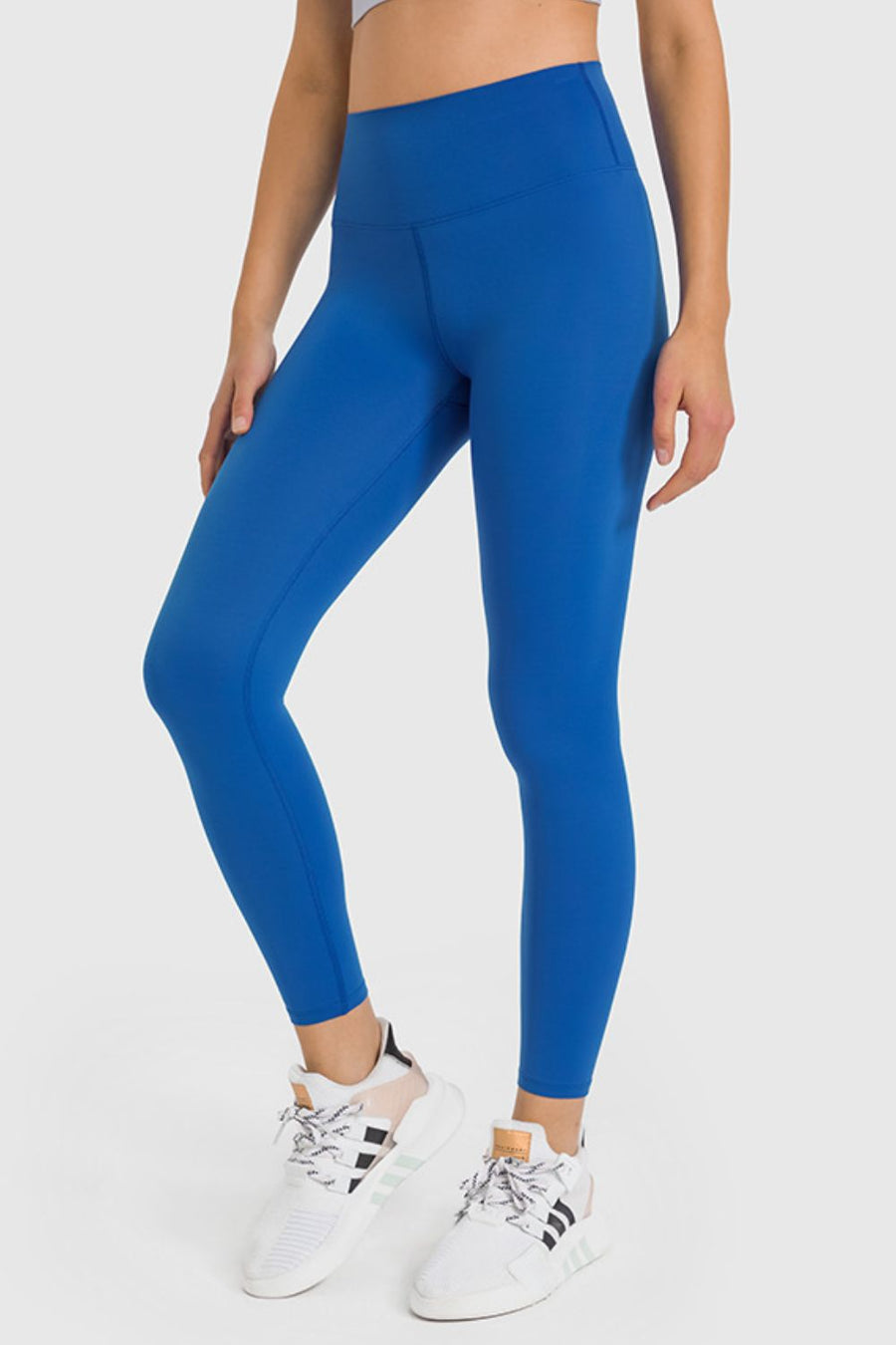 Person wearing blue leggings and white sneakers on a light gray background