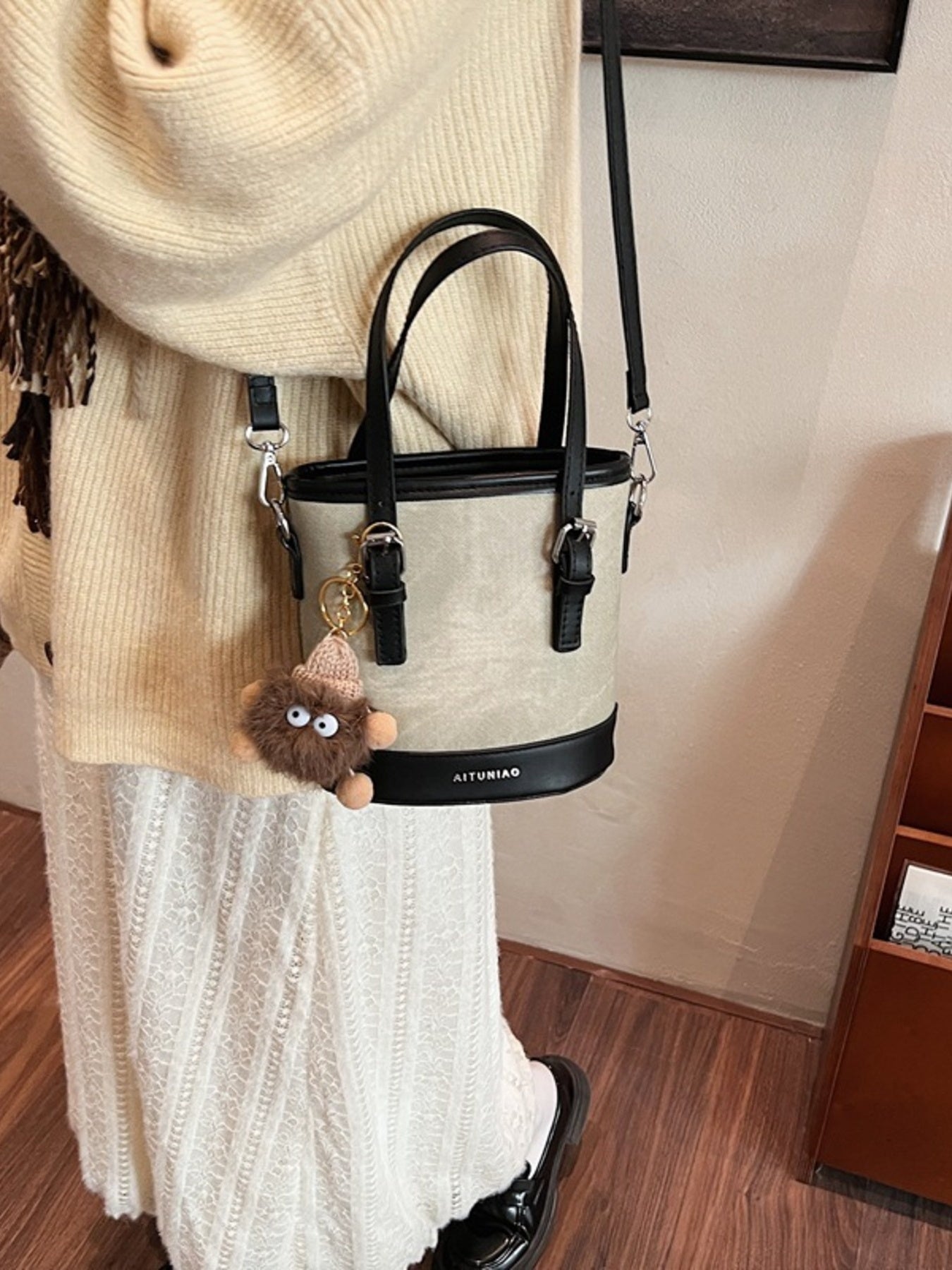 Black and beige handbag with a keychain, hanging on a coat rack.