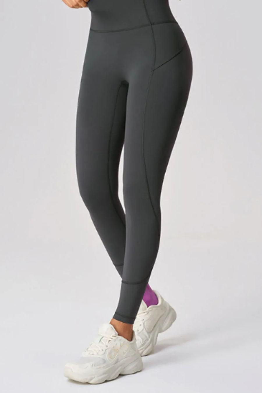Person wearing dark gray leggings and white sneakers on a light gray background