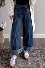Person wearing blue striped pants with a white sweater and sneakers indoors.