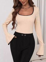 Woman wearing a beige long-sleeve top and black pants against a neutral background