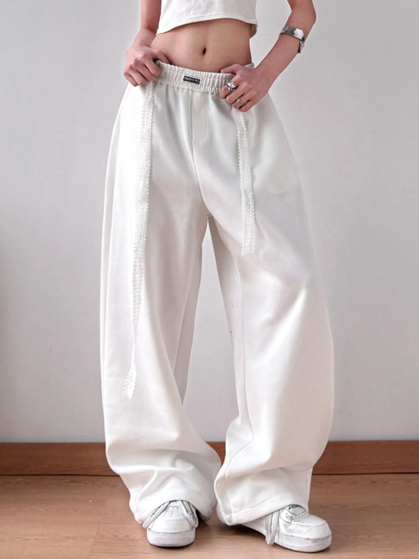 Person wearing white wide-leg pants and white sneakers on a plain background