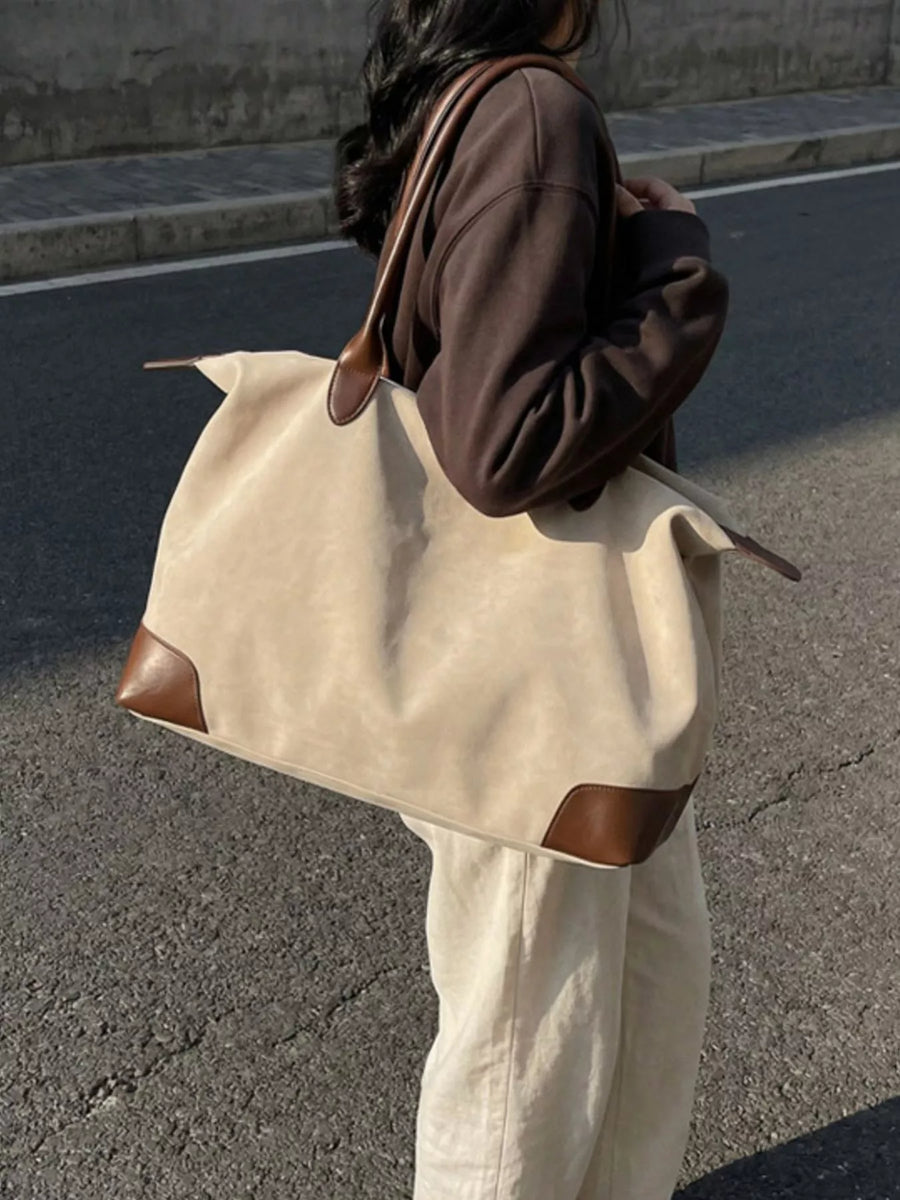 Person carrying a large beige tote bag with brown accents on a street.