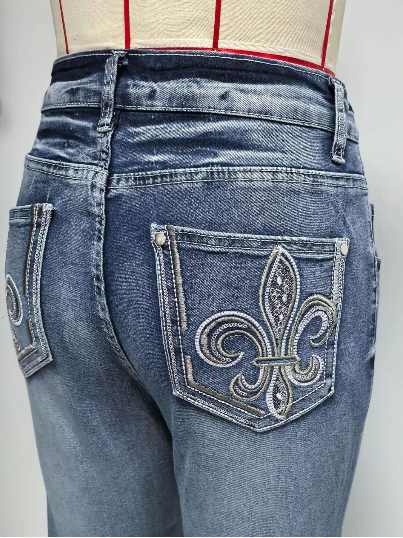 Blue jeans with a decorative fleur-de-lis pocket on a plain background