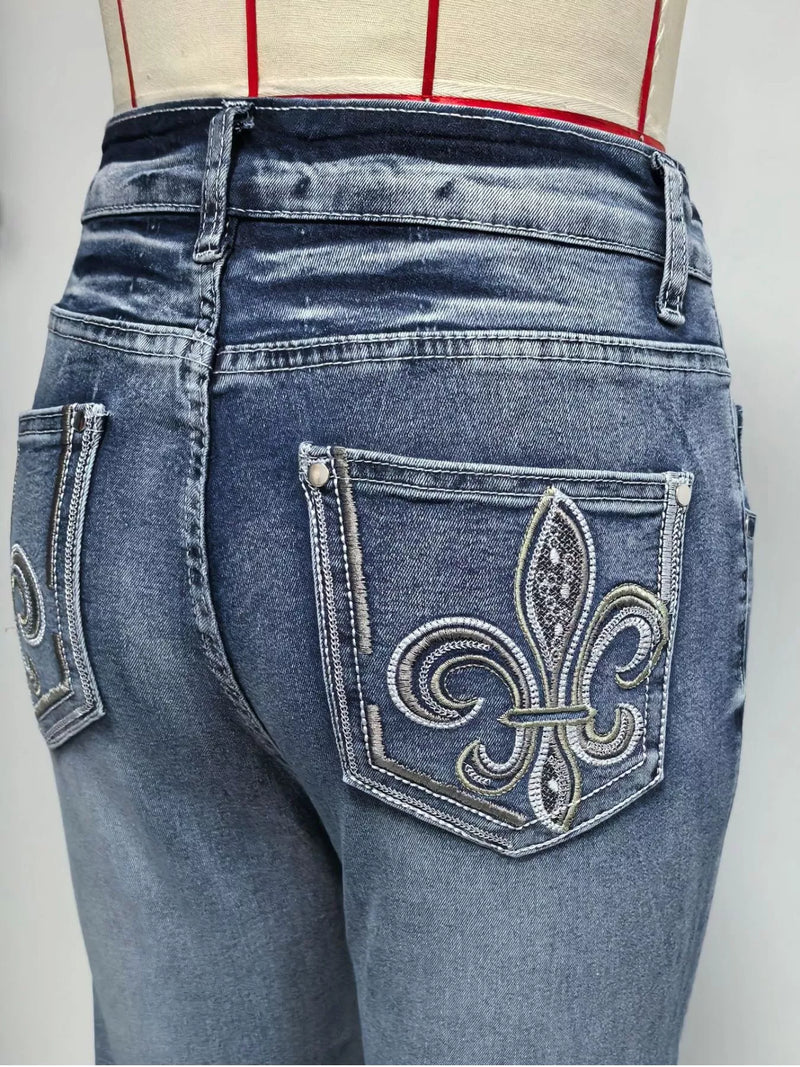 Blue jeans with a decorative fleur-de-lis pocket on a plain background