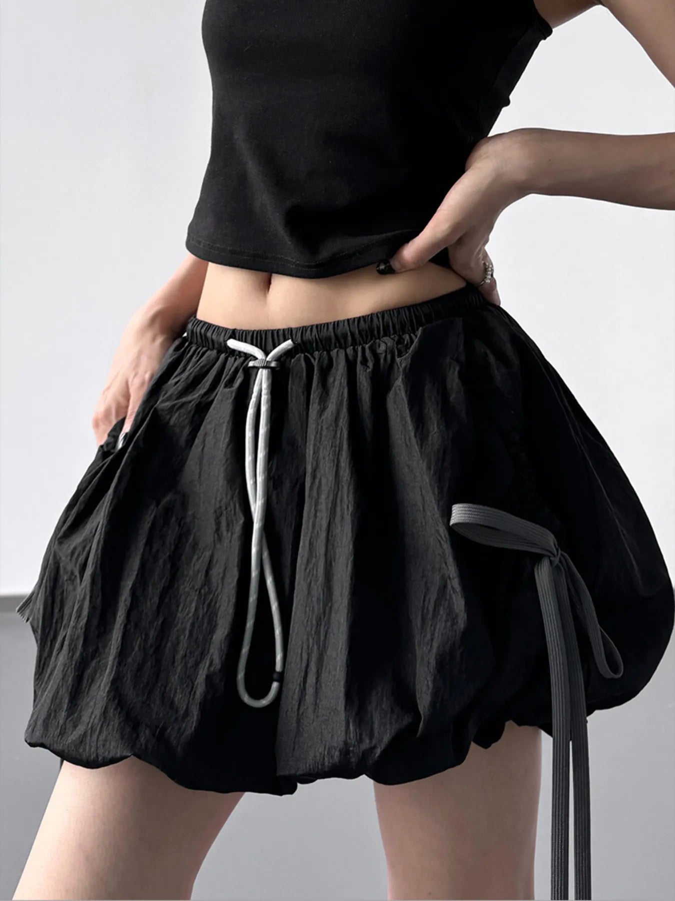 Person wearing black shorts with a drawstring on a plain background