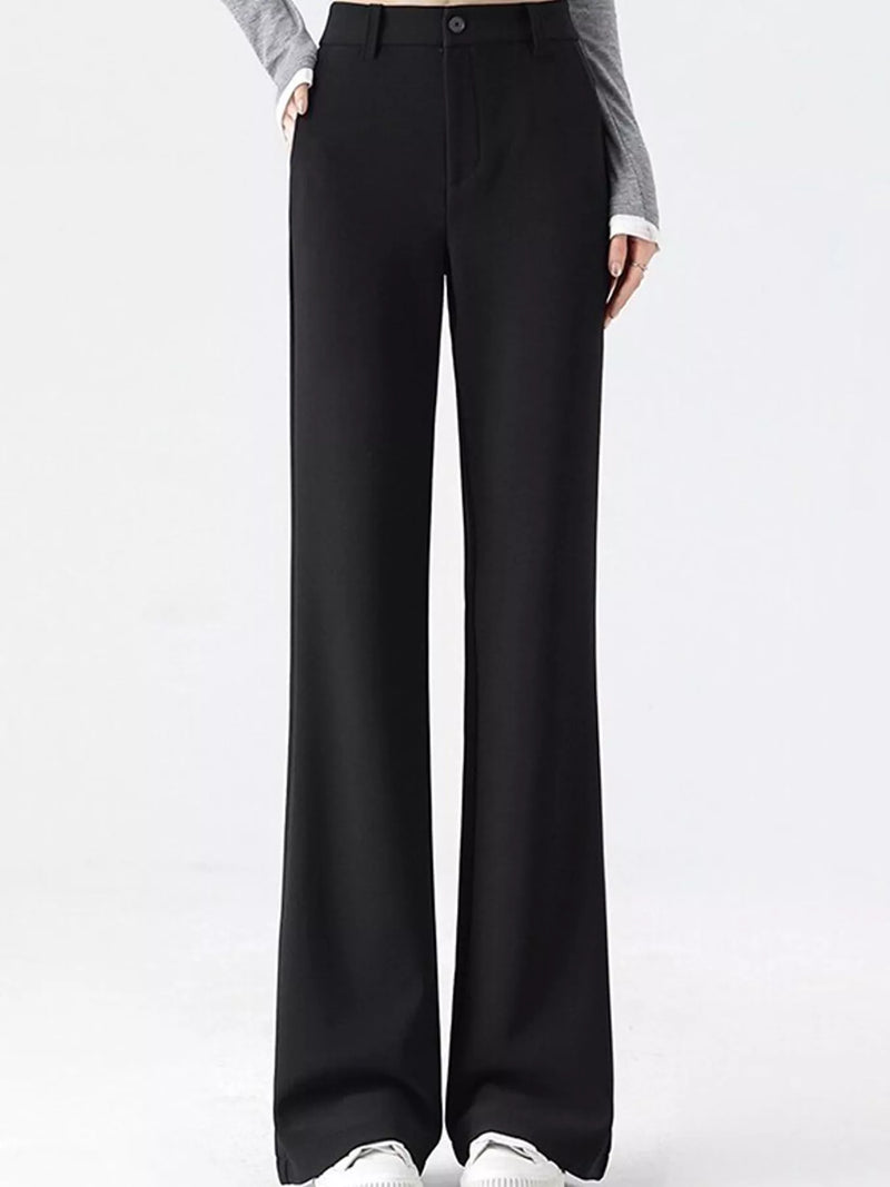 Black wide-leg trousers shown on a model from the waist down, paired with a gray long-sleeve top and white sneakers against a plain white studio background.