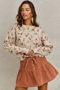 Woman wearing a floral blouse and brown skirt against a neutral background