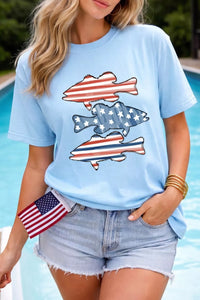 Person wearing a light blue t-shirt with fish designs featuring the American flag, standing by a pool.