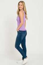 Woman wearing a purple tank top and blue jeans on a white background