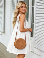 Woman in a white dress holding a round woven bag in front of a white building.