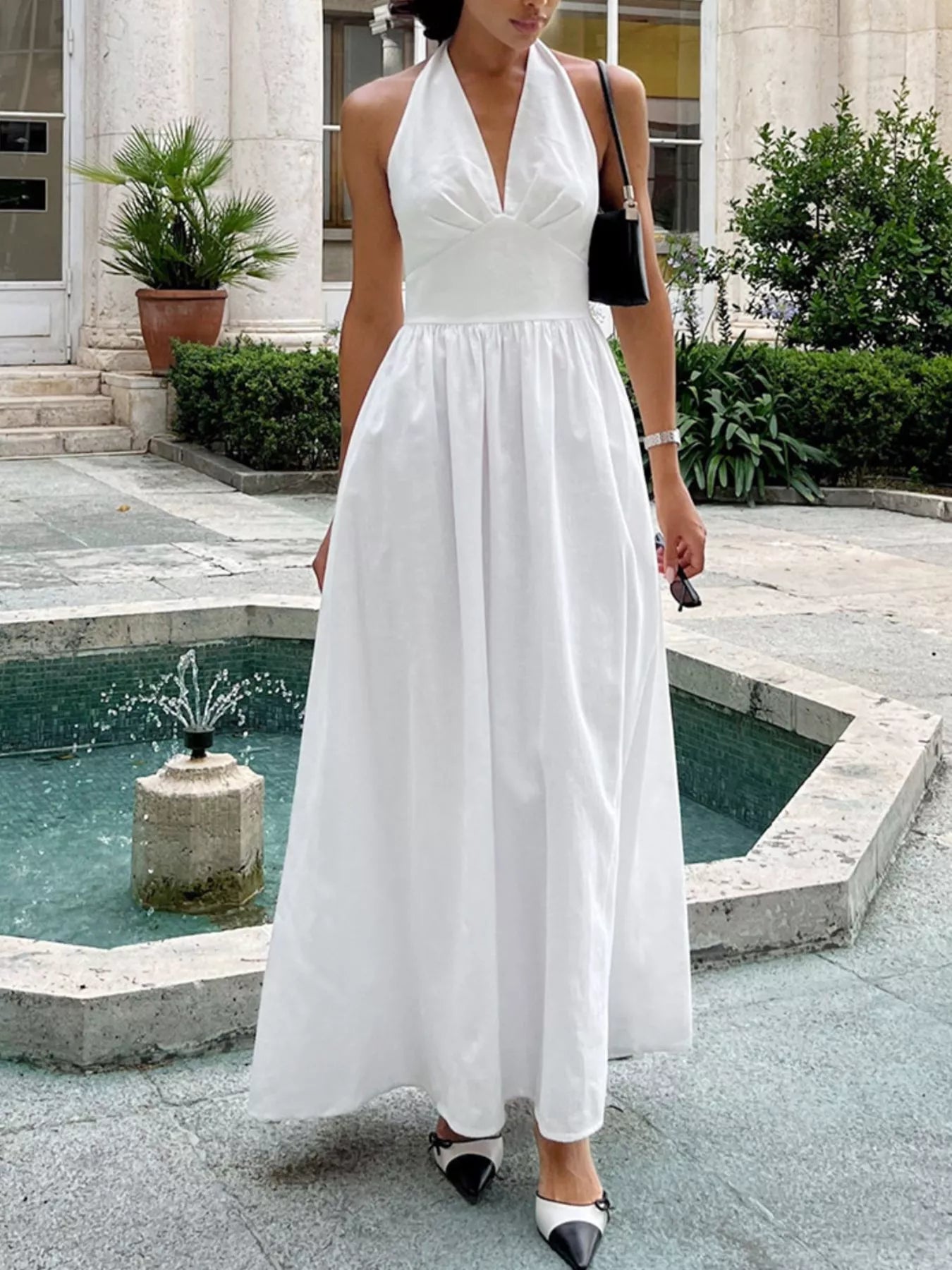 Woman in a white dress standing by a fountain in an outdoor setting