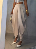 Person wearing a white top and beige high-waisted pants with white shoes, holding a gold clutch.