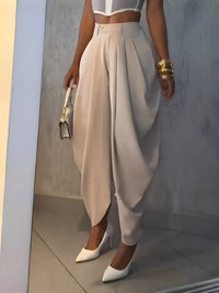 Person wearing a white top and beige high-waisted pants with white shoes, holding a gold clutch.