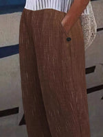 A close-up of a person wearing brown wide-leg trousers with a subtle vertical textured stripe pattern, paired with a white and navy striped top.