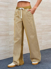 Person wearing beige corduroy pants with a drawstring against a beige wall.