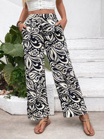 Person wearing black and white patterned pants standing in front of a white wall with green plants.