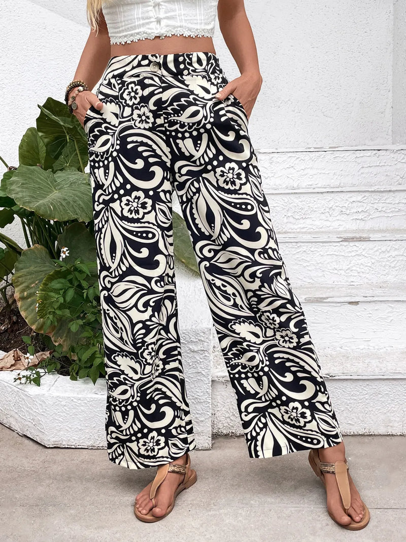 Person wearing black and white patterned pants standing in front of a white wall with green plants.