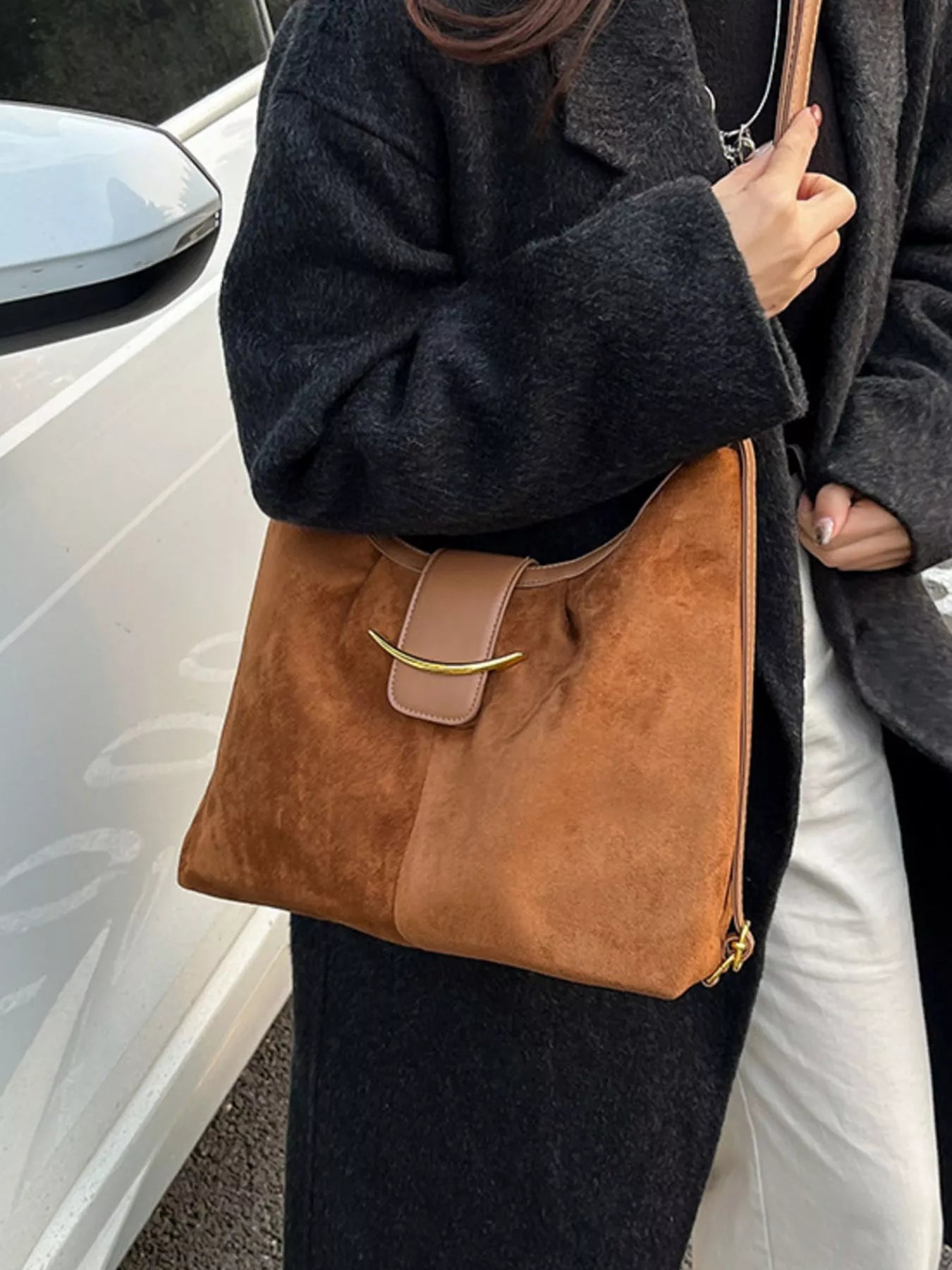 Person holding a brown handbag next to a white car